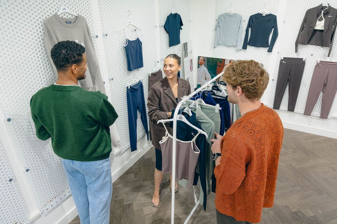 Three colleagues discussing clothing samples in a workspace with activewear displayed on the walls.