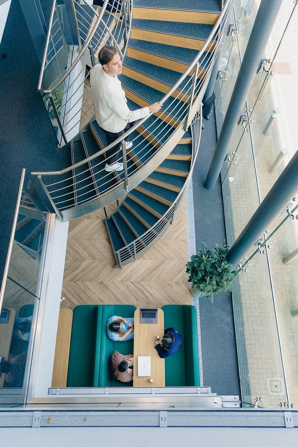 Upward view of people leaning over a spiral staircase railing beneath a glass dome ceiling.
