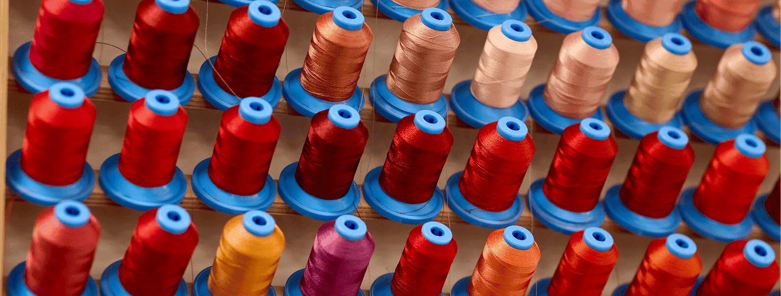 Close-up view of rows of colourful thread spools arranged neatly on a wooden rack, showcasing a variety of vibrant shades.