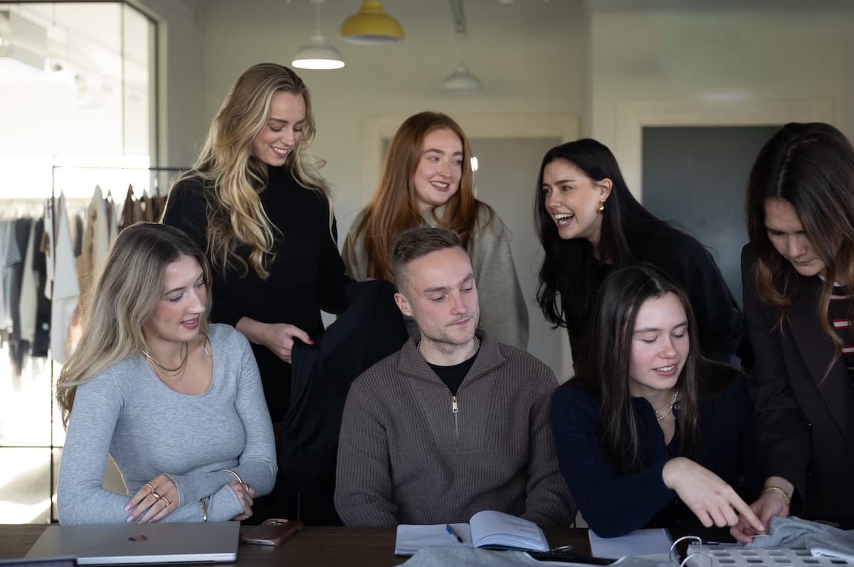 Group of people gathered around a table, examining fabric swatches and samples in a well-lit design studio.