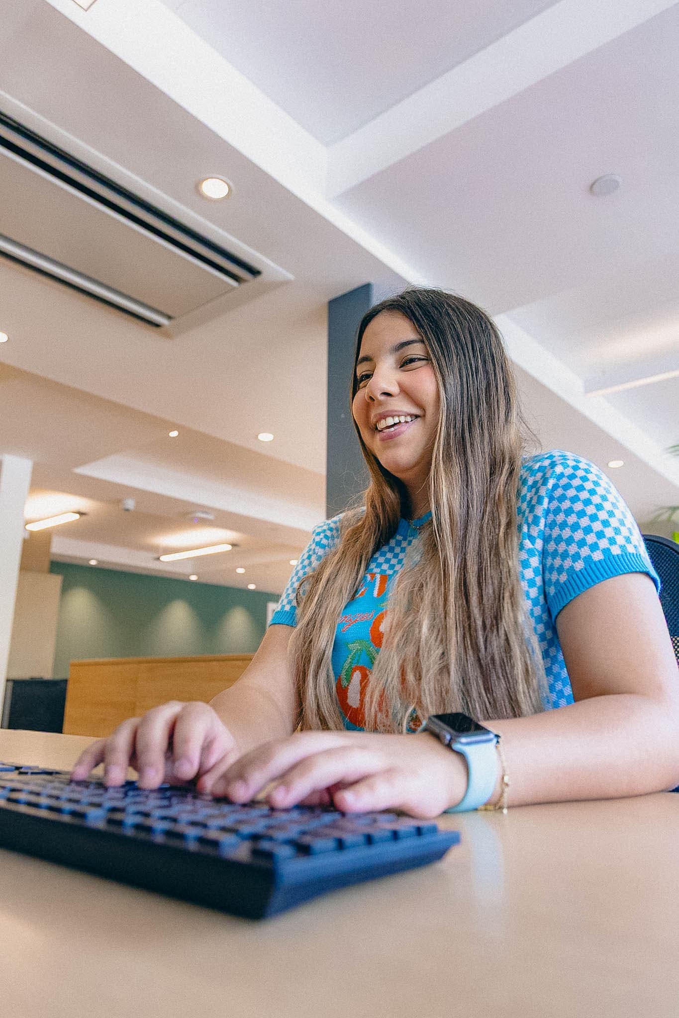 Woman typing on a keyboard, smiling while working at a desk in a modern office setting.